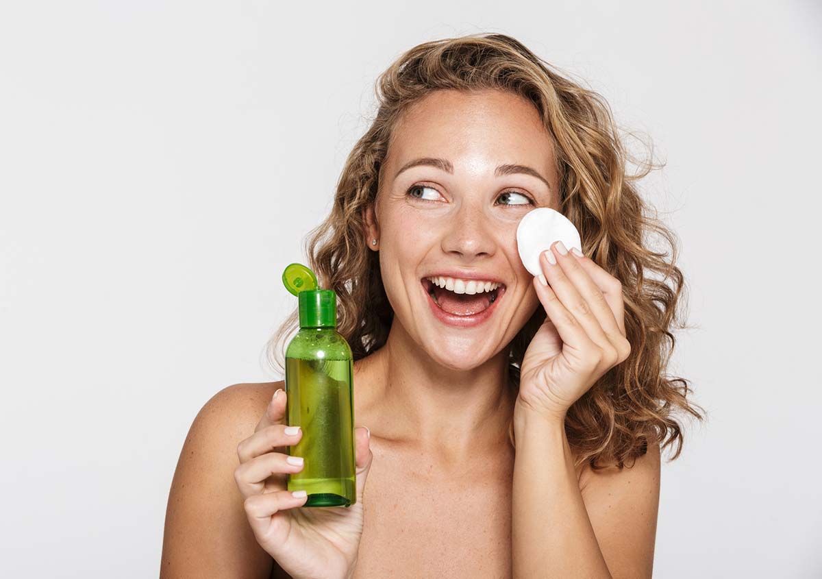 Image of nice half-naked woman laughing and using facial lotion
